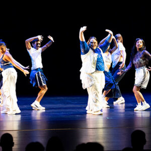 Students in blue and white dance on stage.