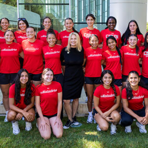 Student athletes dressed in red shirts pose for a group photo on the grass with CSUN President Erika D. Beck.