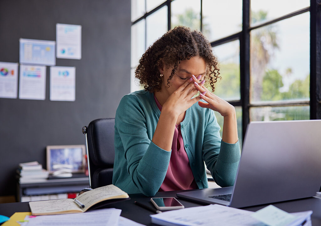 exhausted businesswoman feeling stressed, holding her head while working on a laptop.