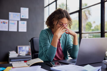 exhausted businesswoman feeling stressed, holding her head while working on a laptop.