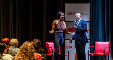 Yan Searcy stands on stage with a microphone with Tiffany Haddish.